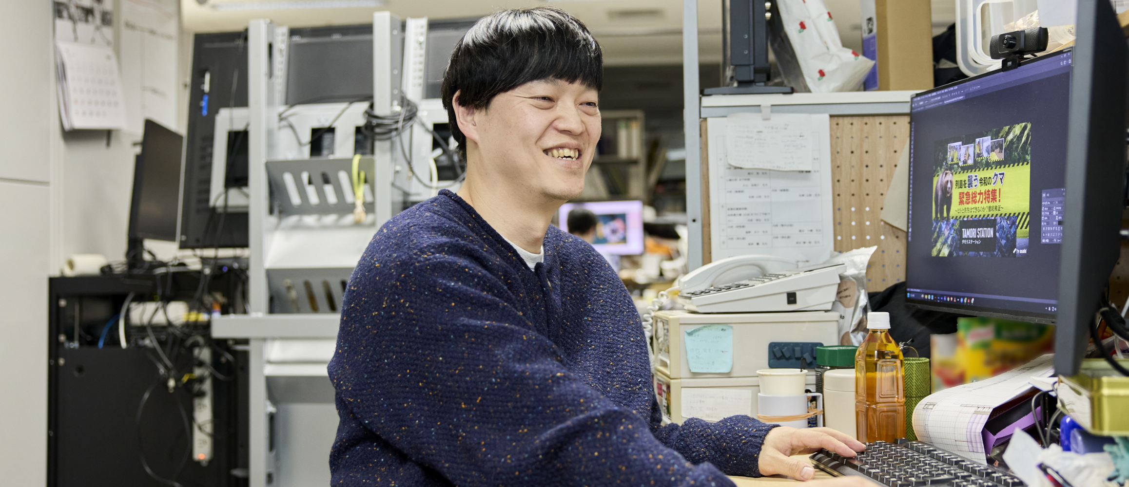 デスクでパソコン作業をしながら、こちらに微笑みかける清野さん。