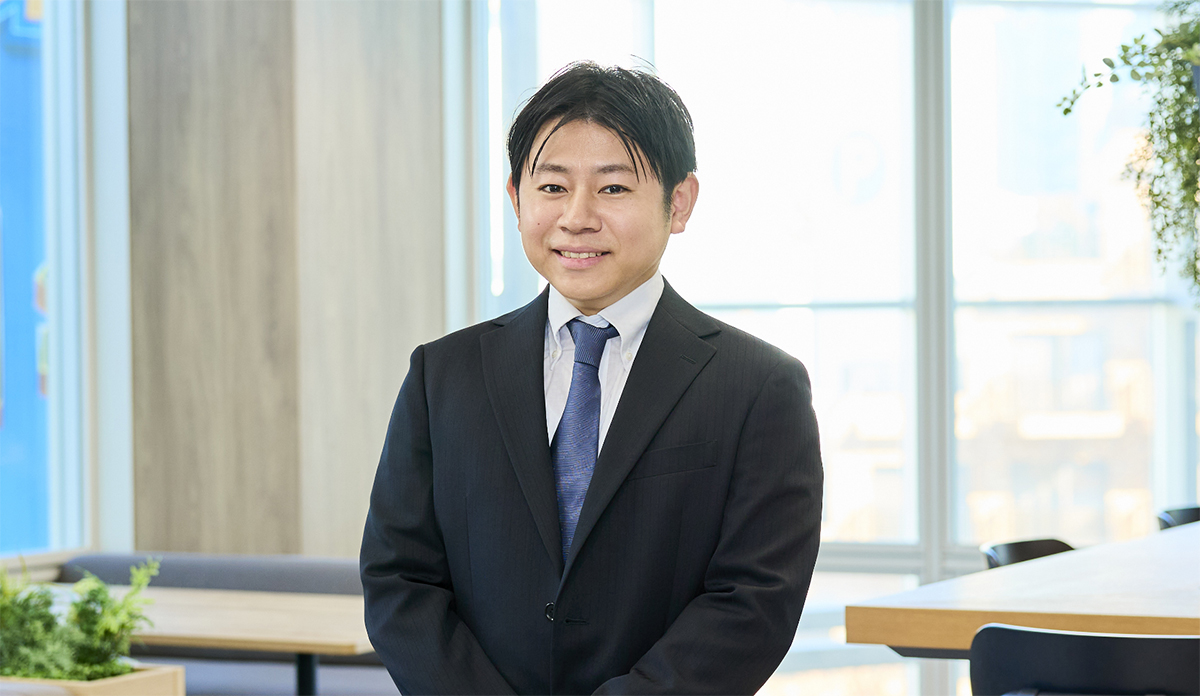 オフィス内のカフェスペースで、微笑む八幡原さんのポートレート写真。