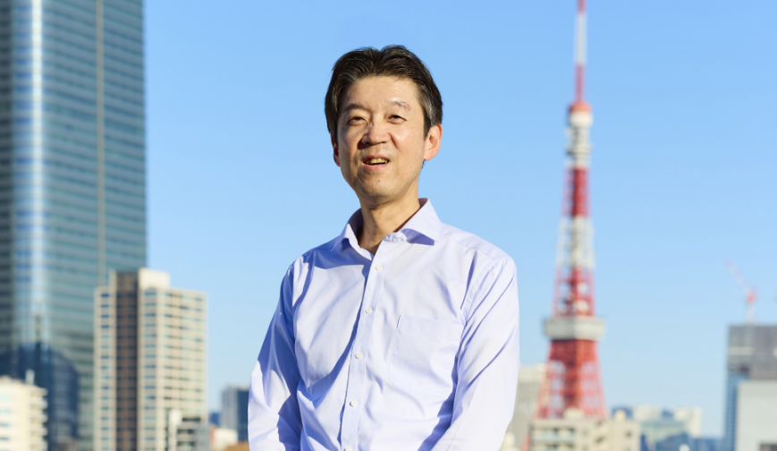 晴天の屋上で微笑む髙島さん。背後には東京タワーが見える。