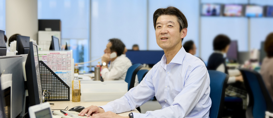 デスクで作業をしながら、笑顔で話をしている髙島さんの様子。